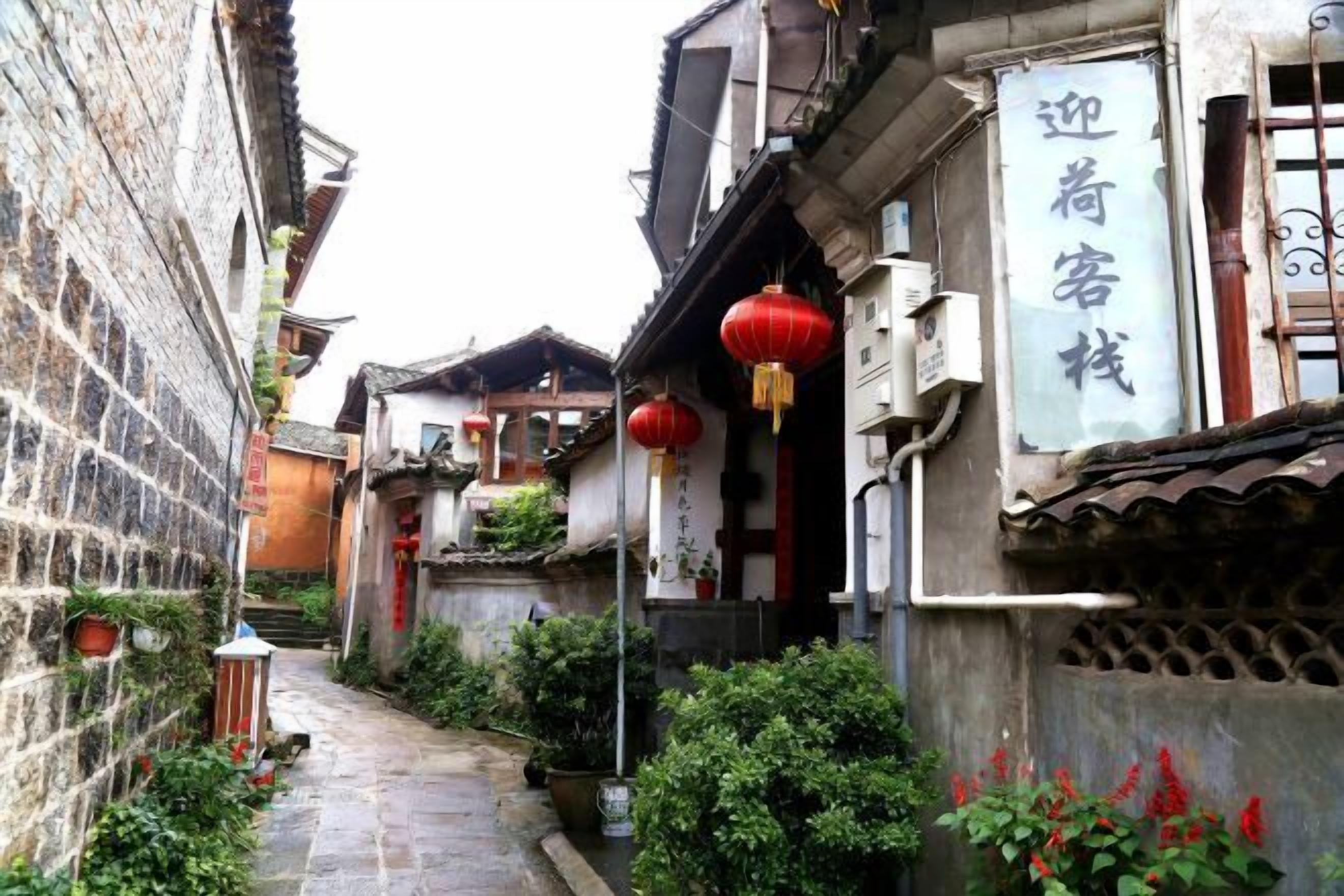 Un estrecho callejón con edificios tradicionales, un letrero y faroles rojos.
