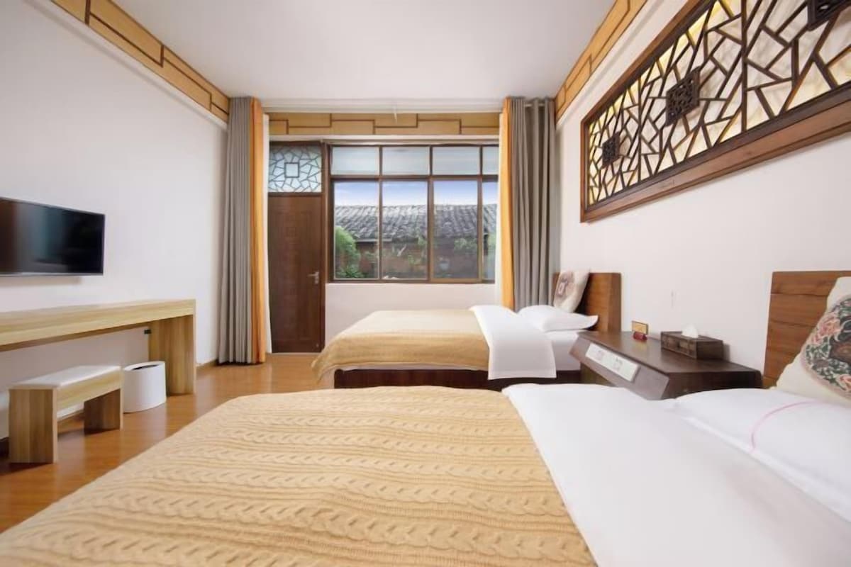 A hotel room with two beds, a flat-screen TV, a wooden desk, and a large window with curtains.