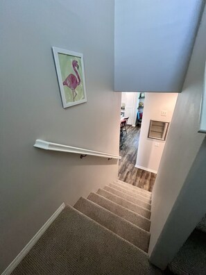 A carpeted staircase with a handrail, a framed picture of a flamingo on the wall, and a glimpse of a kitchen area in the background. - Charming 2-bedroom townhome in Imperial Beach, close to Coronado (Imperial Beach)