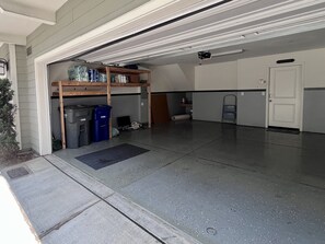 A garage with a wooden shelf stocked with cleaning supplies, a blue trash bin, and a black mat at the entrance. - Charming 2-bedroom townhome in Imperial Beach, close to Coronado (Imperial Beach)