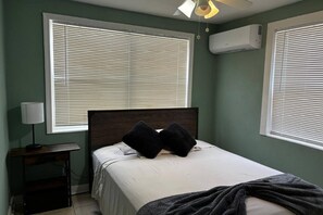A bedroom with a bed, two windows with blinds, a desk with a lamp, and an air conditioner. - Downtown Sarasota 2BR Apartment 2BA Pet Friendly Beaches Sleeps 5 (Sarasota)