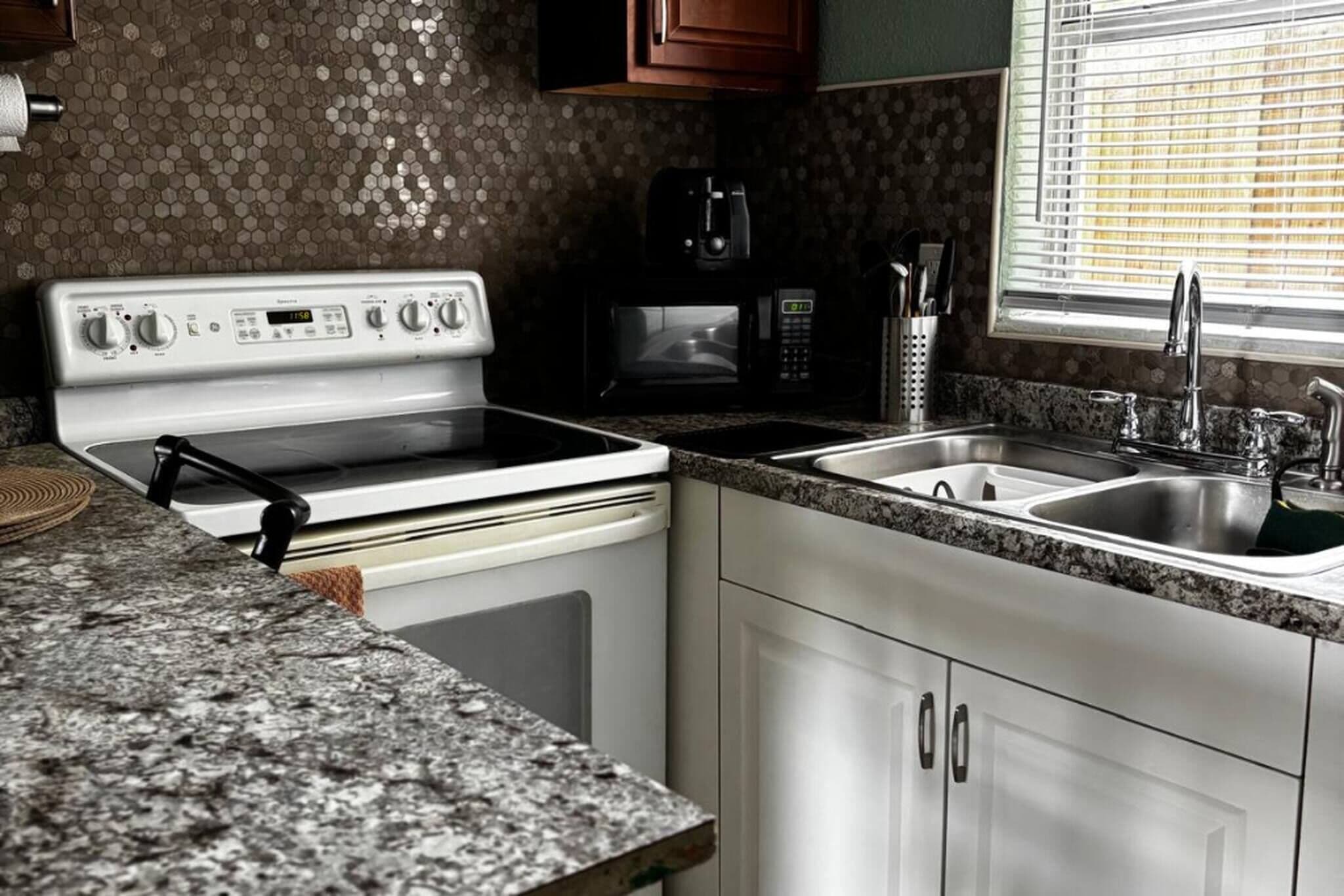 A kitchen with a stove, microwave, sink, and granite countertop.