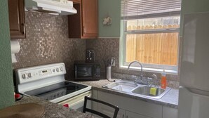 A kitchen with a stove, microwave, sink, and a window with a view of a wooden fence. - Downtown Sarasota 2BR Apartment 2BA Pet Friendly Beaches Sleeps 5 (Sarasota)