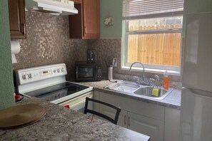 A kitchen with a stove, microwave, sink, and a window with a view of a wooden fence. - Downtown Sarasota 2BR Apartment 2BA Pet Friendly Beaches Sleeps 5 (Sarasota)
