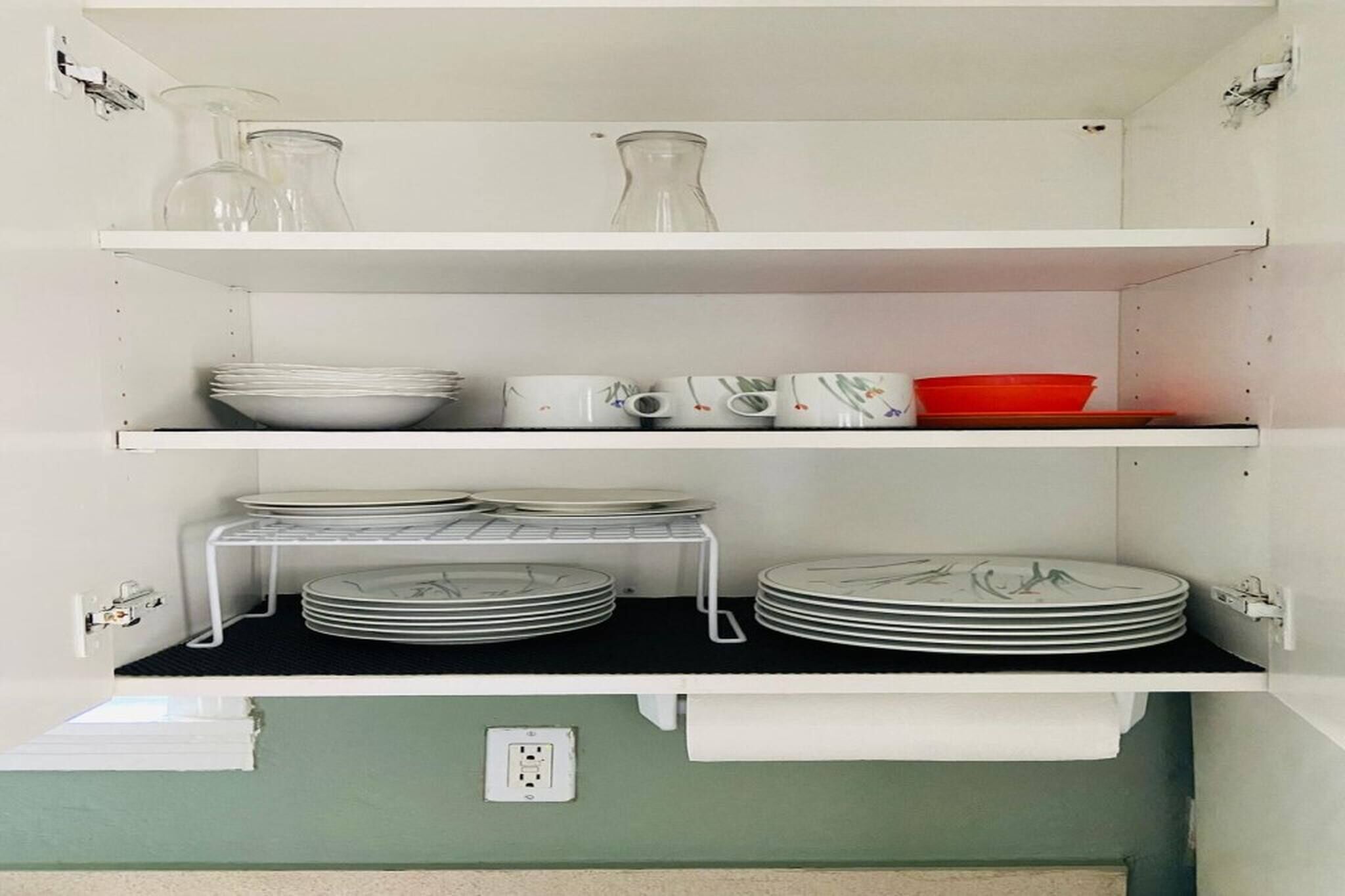 Ein Küchenschrank mit Regalen, auf denen Teller, Schüsseln und ein roter Behälter stehen.