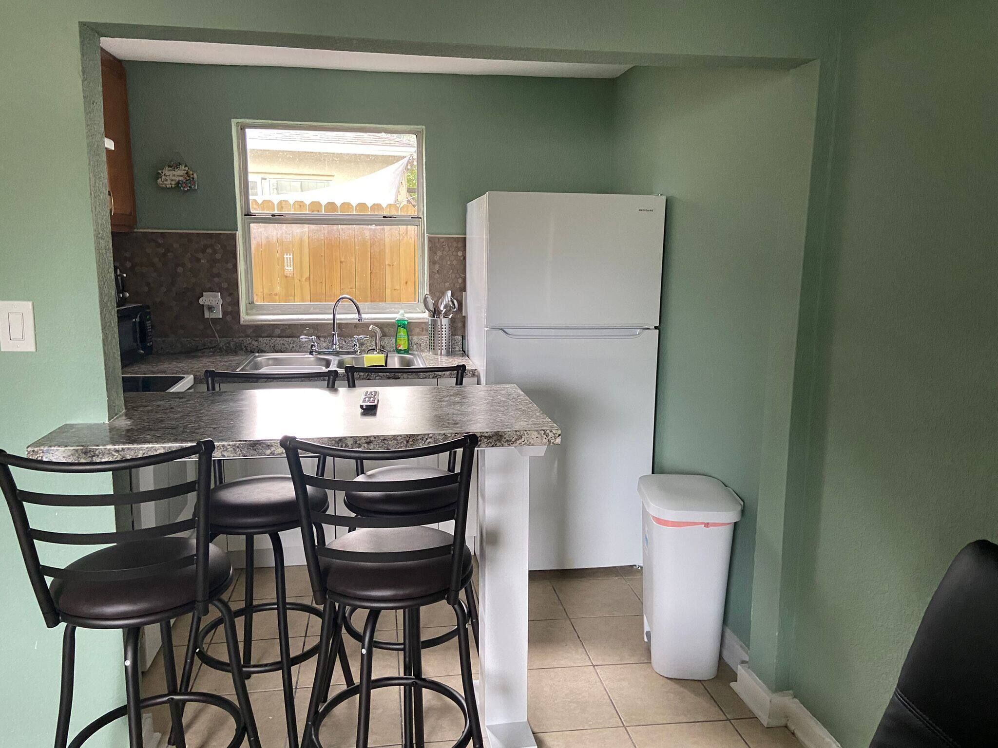 Een kleine keuken met een spoelbak, een koelkast en een eethoek met stoelen.