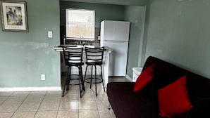 A compact living space with a kitchenette, two bar stools, a couch with red cushions, and a window with blinds. - Downtown Sarasota 2BR Apartment 2BA Pet Friendly Beaches Sleeps 5 (Sarasota)