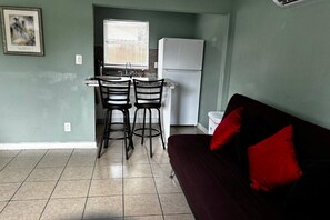 A compact living space with a kitchenette, two bar stools, a couch with red cushions, and a window with blinds. - Downtown Sarasota 2BR Apartment 2BA Pet Friendly Beaches Sleeps 5 (Sarasota)