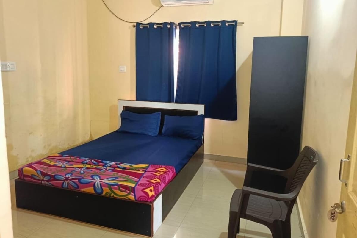 A room with a bed, a chair, a curtain, and an air conditioning unit.