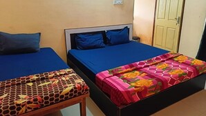 Two single beds with blue bedding, a wooden bench, and a door in a room with beige walls. - Hotel Bindusagar (Bhubaneswar)