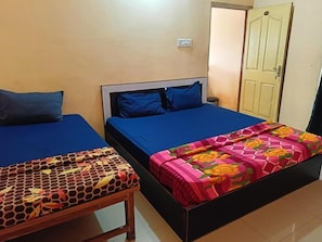 Two single beds with blue bedding, a wooden bench, and a door in a room with beige walls. - Hotel Bindusagar (Bhubaneswar)