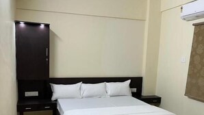 A bedroom with a bed, a ceiling fan, a wardrobe, and a nightstand. - Hotel Bindusagar (Bhubaneswar)