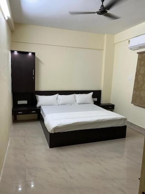 A bedroom with a bed, a ceiling fan, a wardrobe, and a nightstand. - Hotel Bindusagar (Bhubaneswar)