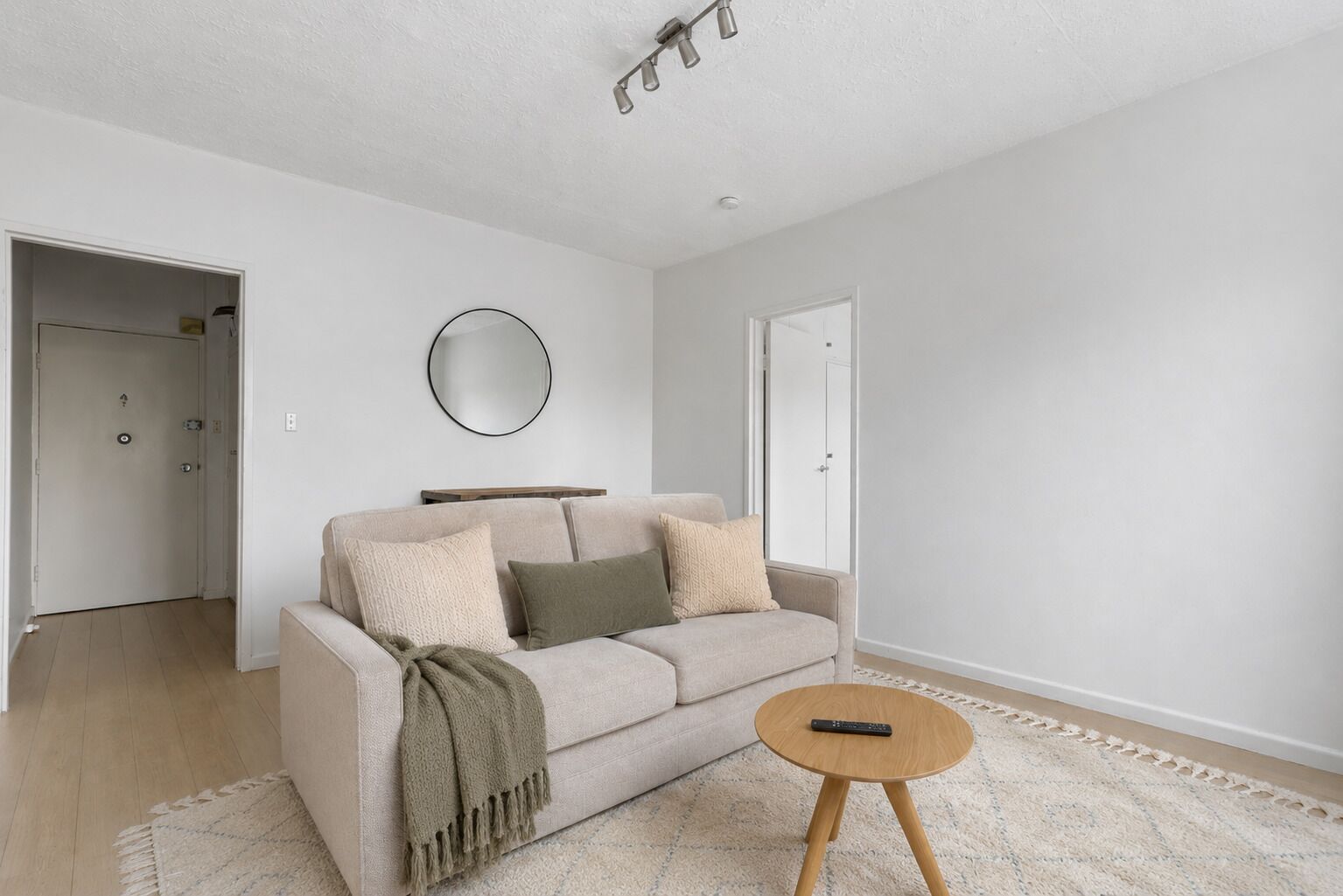 Un salon minimaliste avec un canapé, un miroir rond et une petite table d’appoint en bois.
