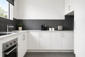 Une cuisine moderne avec des meubles blancs, un évier en acier inoxydable, une machine à café et un grille-pain.