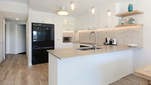 A modern kitchen with white cabinetry, a central island with a sink, and pendant lighting. - Tranquil Waterfront Retreat | Broadbeach Waters (Broadbeach Waters)