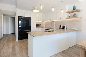 A modern kitchen with white cabinetry, a central island with a sink, and pendant lighting. - Tranquil Waterfront Retreat | Broadbeach Waters (Broadbeach Waters)