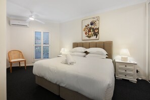 A hotel room with a bed, two bedside tables, a chair, a window with blinds, an air conditioning unit, and a ceiling fan. - Tranquil Waterfront Retreat | Broadbeach Waters (Broadbeach Waters)