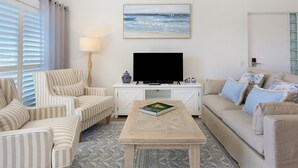 A living room with striped armchairs, a sofa, a coffee table, a flat-screen TV, and a painting of a beach scene. - Tranquil Waterfront Retreat | Broadbeach Waters (Broadbeach Waters)
