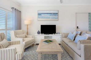 Ein Wohnzimmer mit gestreiften Sesseln, einer Couch, einem Couchtisch, einem Flachbildfernseher und einem Gemälde mit Strandmotiv.