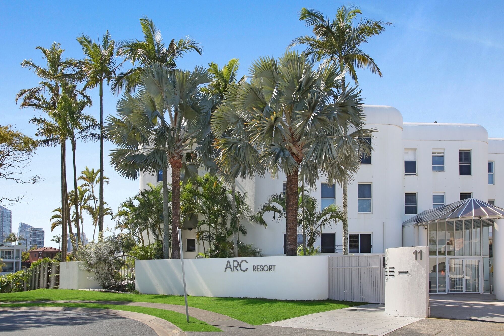 A white building with a sign reading 'ARC RESORT' and palm trees in front.