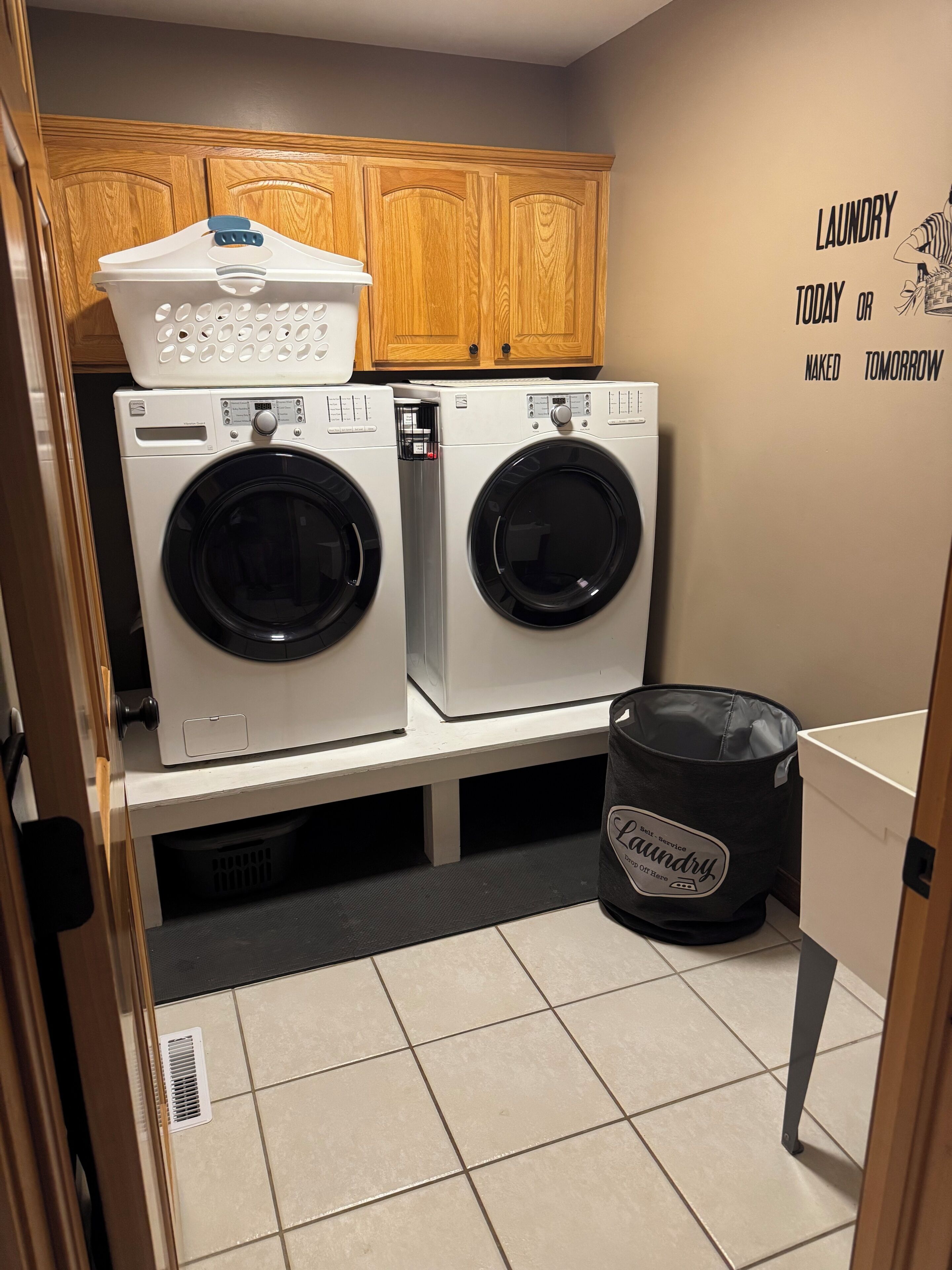 A laundry room with two stacked front-loading washers, a drying rack, and a bag labeled 'Laundry Service.'