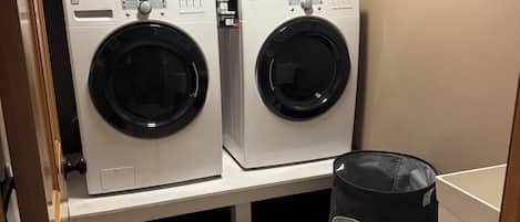 A laundry room with two stacked front-loading washers, a drying rack, and a bag labeled 'Laundry Service.'