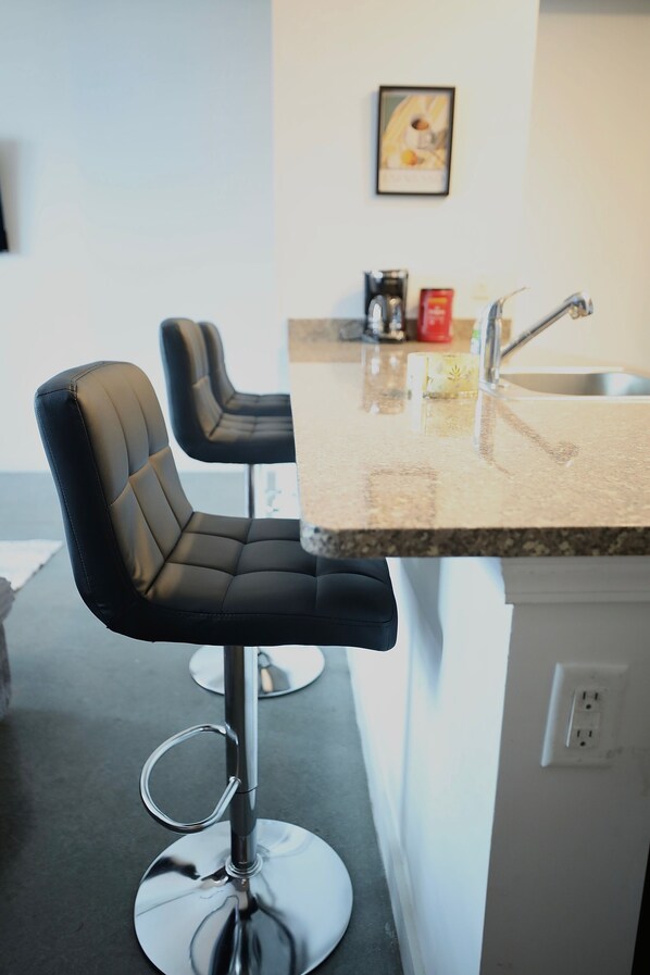 A modern kitchen with a bar stool, a sink, and a coffee maker.