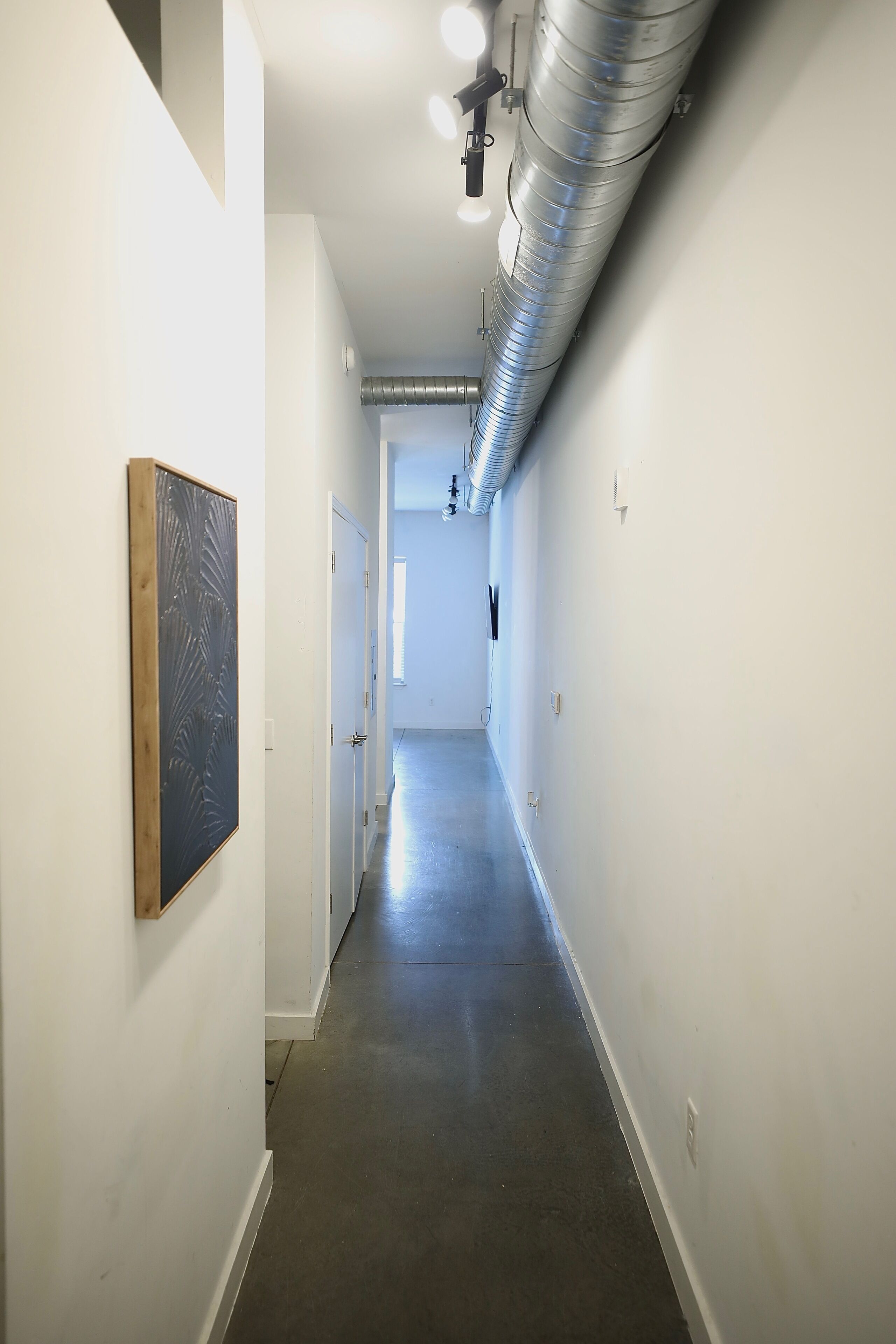 En gang med hvide vægge, et indrammet kunstværk og et loft med ventilationskanaler.