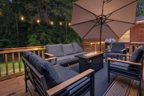 An outdoor patio with a sofa, chairs, a table with a built-in fire feature, and string lights.