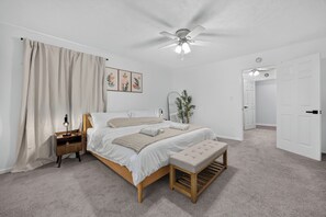 Ein Schlafzimmer mit Bett, Nachttisch, Bank, Deckenventilator und einer Tür.