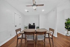 Zona pranzo con tavolo e sedie in legno, ventilatore a soffitto, illuminazione incassata, una porta e una pianta in vaso.