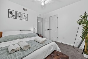 A bedroom with a bed, a bedside table, a wall-mounted artwork, a door, and a potted plant.