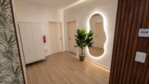 Ein Flur mit Holzboden, einem Blumentopf, einem Spiegel mit Holzrahmen und einer Tür mit Feuerlöscher.