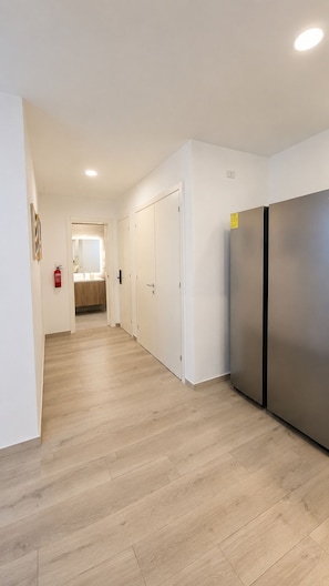 A hallway with a wooden floor, white walls, and a stainless steel refrigerator. - Coral Juliette •Luxury PH in Cocotal • Pool • BBQ (Punta Cana)