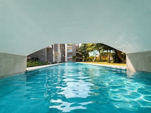 A swimming pool with a view of a building and trees in the background. - Coral Juliette •Luxury PH in Cocotal • Pool • BBQ (Punta Cana)