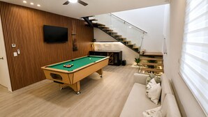 Ein modernes Wohnzimmer mit Billardtisch, einer Couch und einer Treppe.