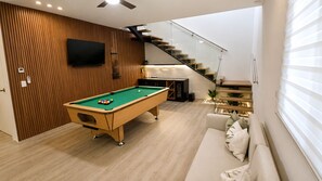 A modern living room with a pool table, a sofa, and a staircase. - Coral Juliette •Luxury PH in Cocotal • Pool • BBQ (Punta Cana)