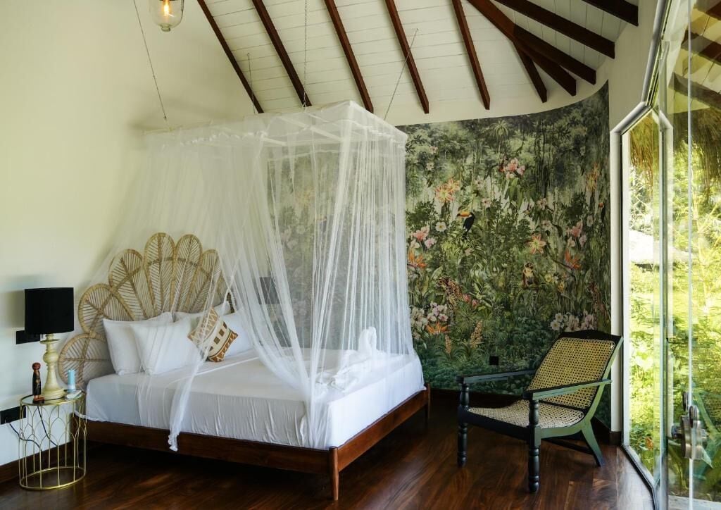 Un dormitorio con cama con dosel, dosel, una silla de ratán y papel tapiz floral.