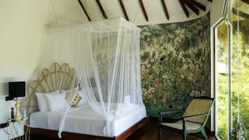 Un dormitorio con cama con dosel, dosel, una silla de ratán y papel tapiz floral.
