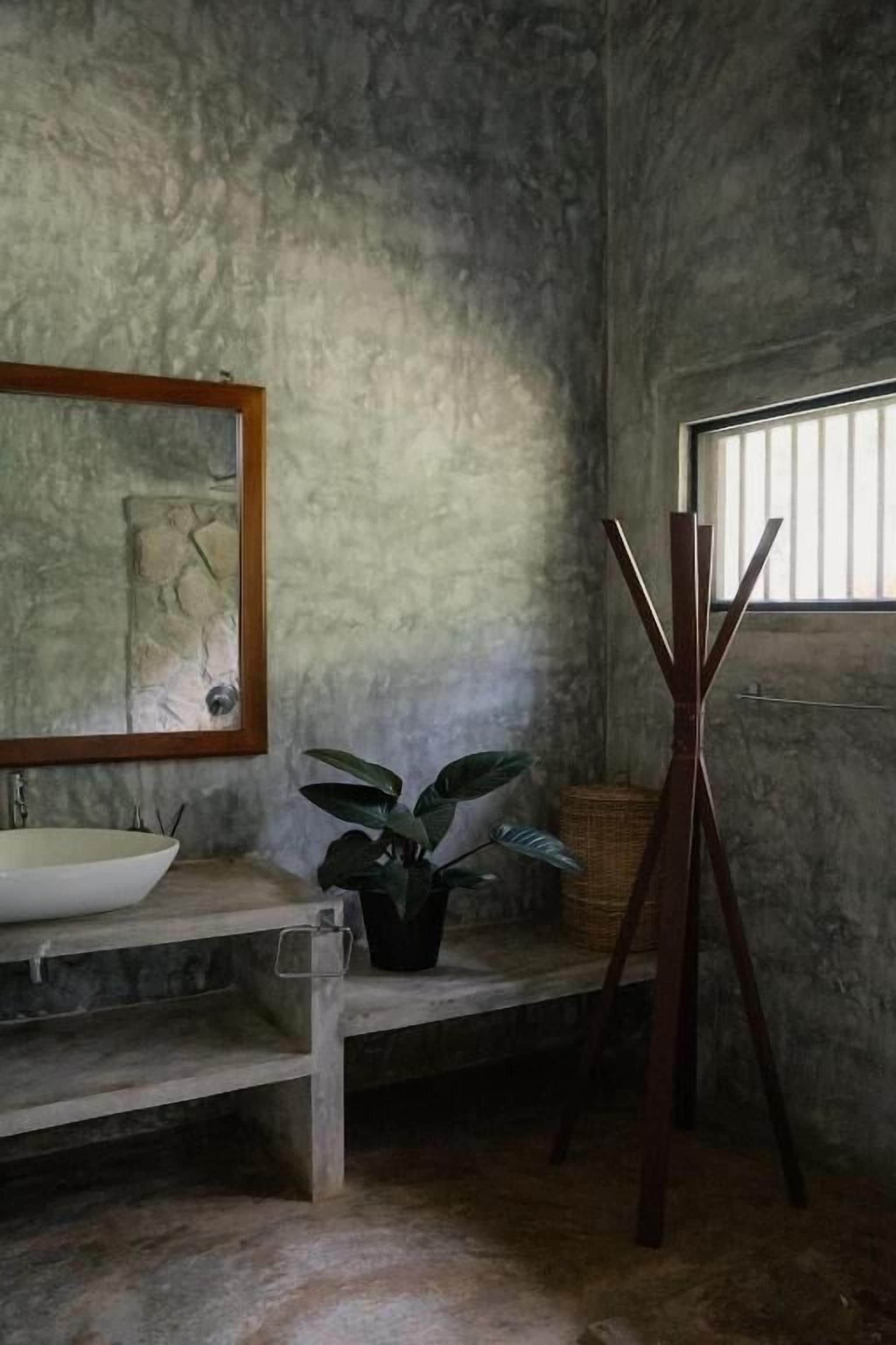 A bathroom with a stone sink, a mirror, a potted plant, and a wooden easel.