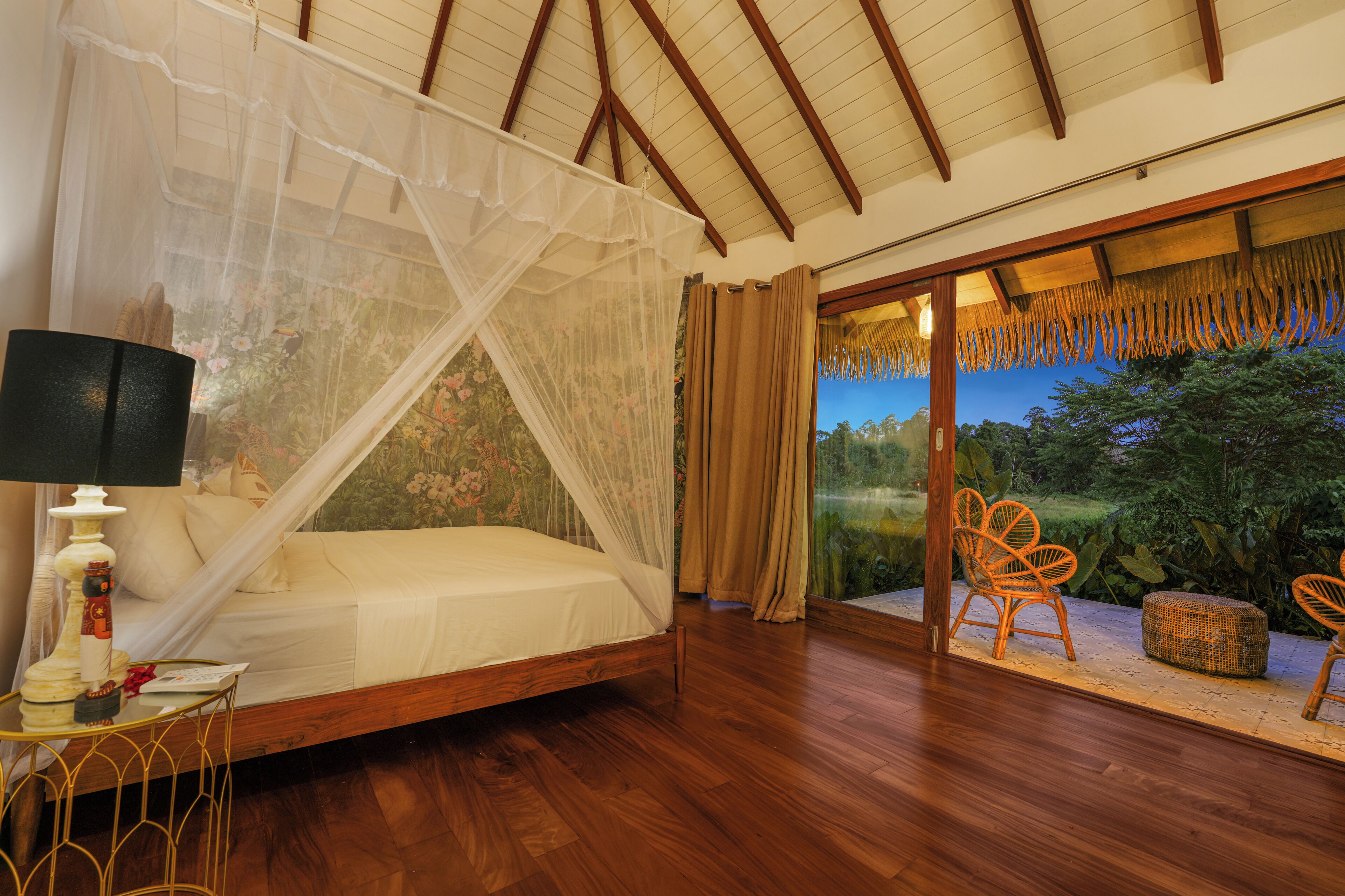 A bedroom with a canopy bed, a nightstand, a lamp, and a view of the outdoors through a glass door.