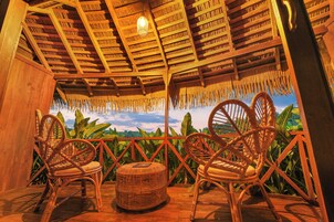 A wooden veranda with wicker furniture and a view of lush greenery.