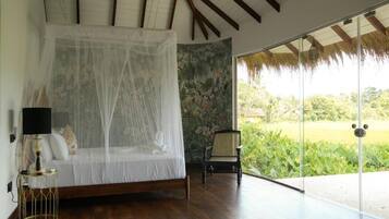 A bedroom with a canopy bed, a chair, and a view of greenery outside.