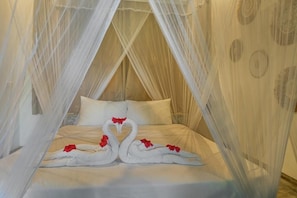 A bed with a canopy, swan-shaped pillows, and red flowers. - Huma Terra Lodge (Hikkaduwa)
