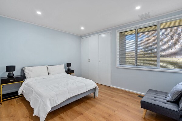 Un dormitorio con cama, mesitas de noche, un armario y una ventana con persianas.