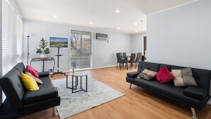 A modern living room with a black sofa, a small round table, and a dining area with chairs. - Family-Friendly 3-Bed House in Kambah (Kambah)