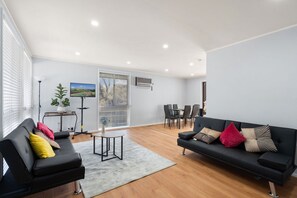 A modern living room with a black sofa, a small round table, and a dining area with chairs. - Family-Friendly 3-Bed House in Kambah (Kambah)