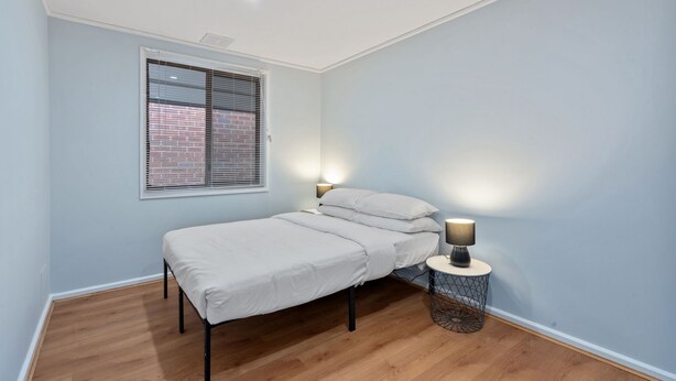 A bedroom with a single bed, a window with blinds, a bedside lamp, and a round side table. - Family-Friendly 3-Bed House in Kambah (Kambah)