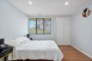 Ein Schlafzimmer mit einem Bett, einem Nachttisch, einem Fenster mit Jalousien und einer Tür.